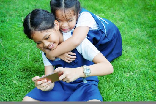 two little sister girls playing internet with mobile smartphone on grass