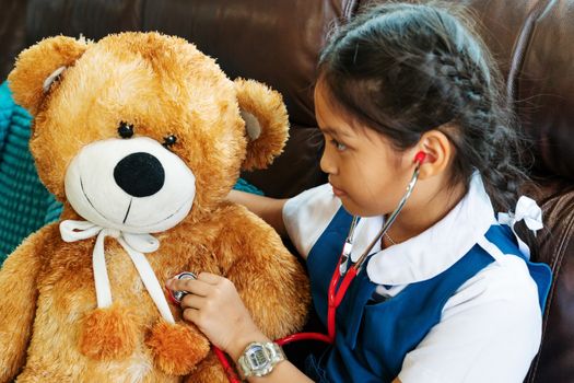 little girl is smiling and playing doctor with brown bear and stethoscope. Kid and health care concept.