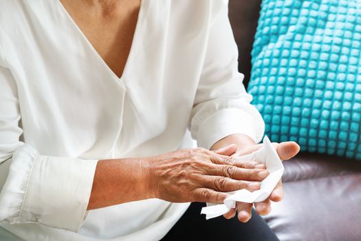 old woman cleaning her hands with white soft tissue paper at home