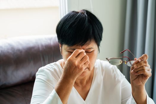 Tired old woman removing eyeglasses, massaging eyes after reading paper book. feeling discomfort because of long wearing glasses, suffering from eyes pain or headache