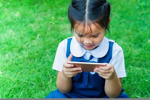 cute little girls playing internet with mobile smartphone on grass
