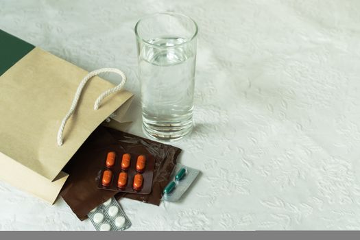 Prescription order from hospital doctor with medicines, drug in plastic zip bags for chronic patient with glass of water on white background.