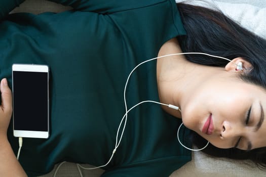 Over head view of beautiful young woman laying down on sofa using smartphone to listen the music