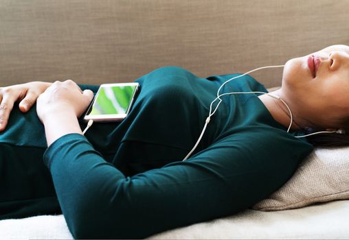 Over head view of beautiful young woman laying down on sofa using smartphone to listen the music