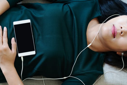 Over head view of beautiful young woman laying down on sofa using smartphone to listen the music