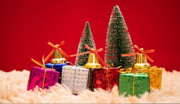 Christmas background concept. Christmas gift box and tree with golden bells, pine cones, red and white ball on red background