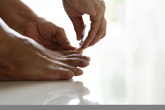 nail clipping, senior woman foot cutting nails using nail clipper on white background, closeup