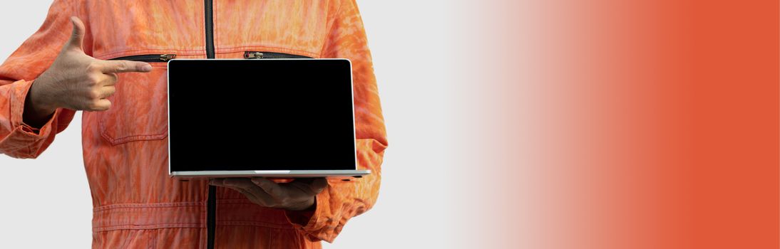 The chief mechanic in an orange uniform holding blank screen laptop. Standing with his finger point to computer. Portrait with studio light.