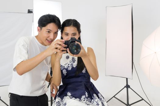 Asian photographers allow models to view pictures taken on the camera screen. The young model is very satisfied with her photo. The atmosphere in the photo studio.