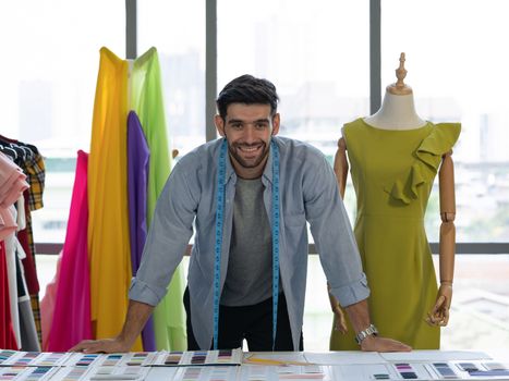 Young fashion designer is ready to work on a table full of brightly colored fabric samples. Morning atmosphere in the tailor's shop.