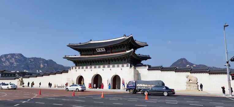A wide angle view of the gyeongdong palace gate making an interesting mix of the heritage traditional structure and the modern structure and vehicles