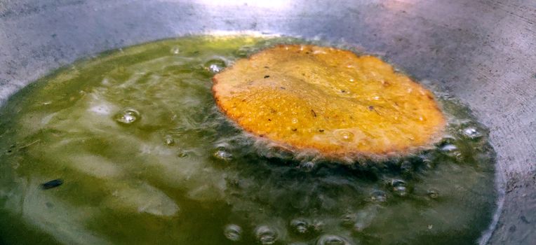 Close up of deep fried Indian bread called Puri in a cooking pan with vegetable oil