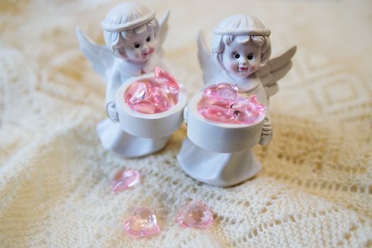 Two white ceramic angel figurines with baskets with pink hearts on a light background. Angel figurine for concept design. The concept of love and kindness.