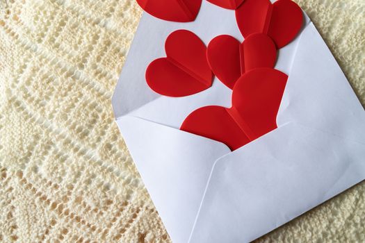 Red hearts and a white mail envelope on a background of knitted texture. Love heart frame. Happy mother's day concept. Love symbol. Holiday card background, copy space for text.