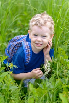 A little boy in a blue butcher crouched in green grass