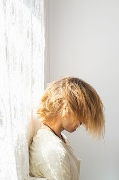 Young man with medium long blonde hair frustrated at not being able to leave home. Looking down on a white background. Loneliness and silence concept.