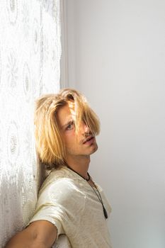 Young man with medium long blonde hair frustrated at not being able to leave home. Looking towards the camera on a white background. Loneliness and tiredness concept.