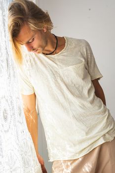 Young man with medium long blonde hair frustrated at not being able to leave home. Looking down on a white background. Loneliness and silence concept.