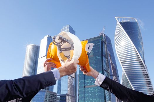 Group of business people clinking their helmets as a success on skyscrapers background, construction finished concept