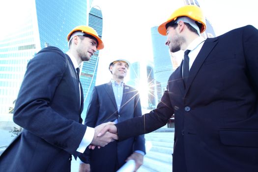 Architect and engineers shaking hands at construction site, skyscrapers on background