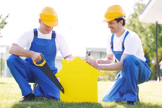 Workers with yellow house model building construction concept