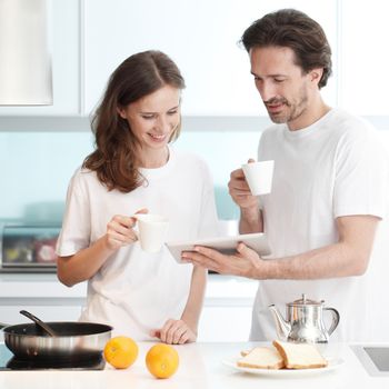 Couple cooking breakfast together in kitchen using tablet pc