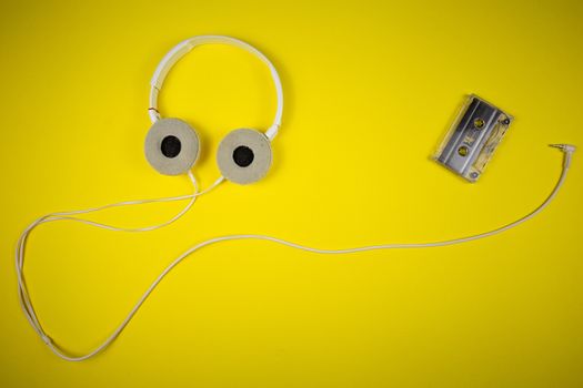 Audio cassette tape and modern headphones on a yellow background, music