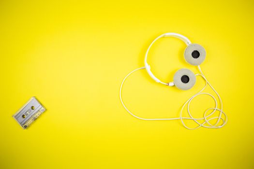 Audio cassette tape and modern headphones on a yellow background, music