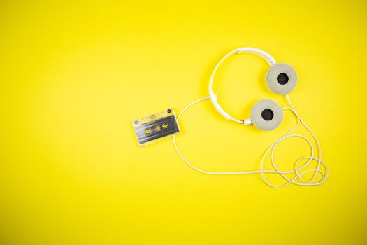 Audio cassette tape and modern headphones on a yellow background, music