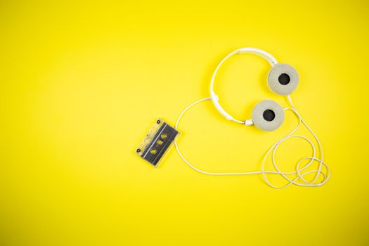 Audio cassette tape and modern headphones on a yellow background, music