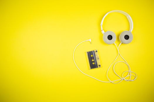 Audio cassette tape and modern headphones on a yellow background, music