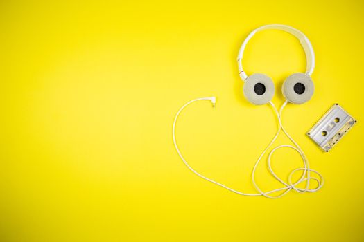 Audio cassette tape and modern headphones on a yellow background, music