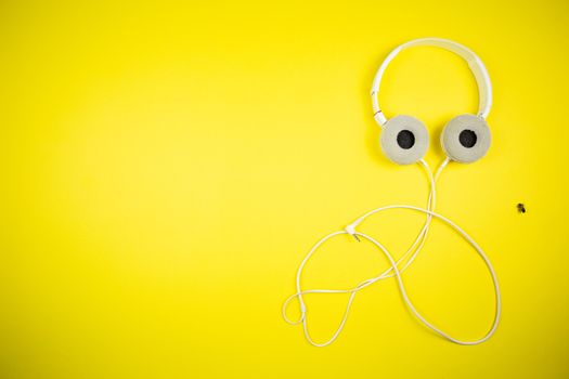 White audio headphones with a 3.5 mm wire on a yellow background, music