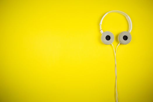 White audio headphones with a 3.5 mm wire on a yellow background, music