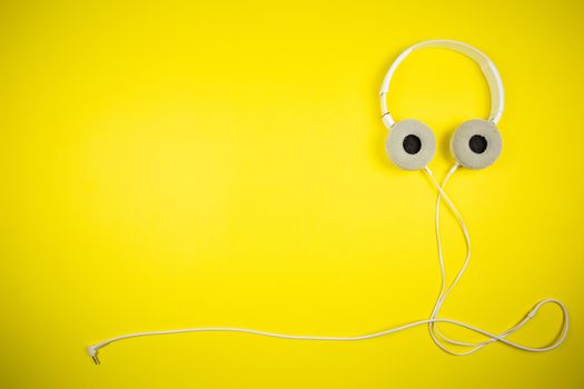 White audio headphones with a 3.5 mm wire on a yellow background, music