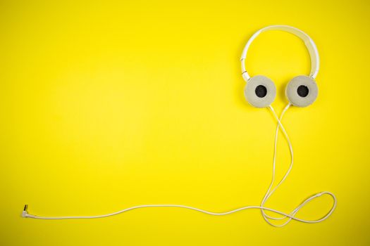 White audio headphones with a 3.5 mm wire on a yellow background, music