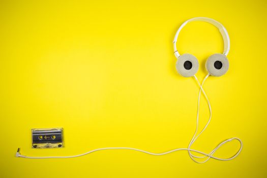 Audio cassette tape and modern headphones on a yellow background, music