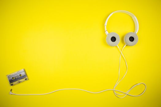 Audio cassette tape and modern headphones on a yellow background, music