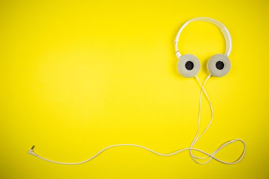 White audio headphones with a 3.5 mm wire on a yellow background, music