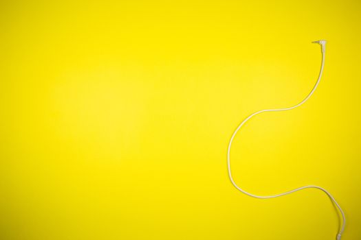 White 3.5mm audio cable from headphones on a yellow background, tehnology