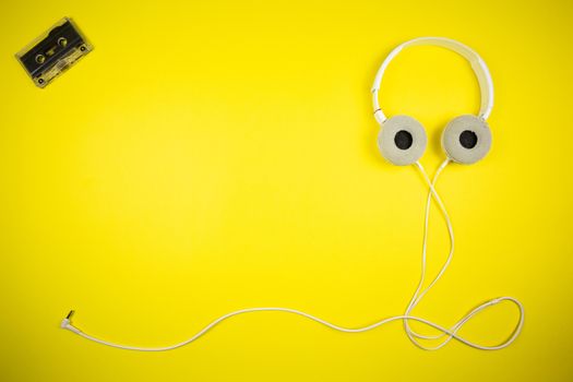 Audio cassette tape and modern headphones on a yellow background, music