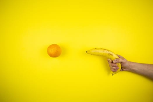 Banana shoots an orange on a yellow background, fruits
