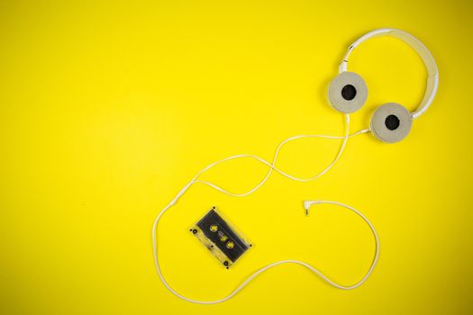 Audio cassette tape and modern headphones on a yellow background, music