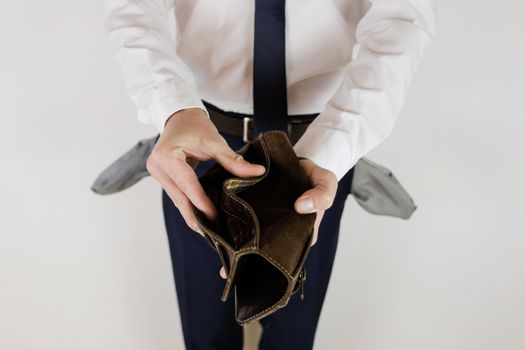 A man in a business suit holds in his hands an empty wallet without money. Financial crisis. Bankruptcy in business. The employer is disappointed.