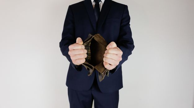 A man in a business suit holds in his hands an empty wallet without money. Financial crisis. Bankruptcy in business. The employer is disappointed.