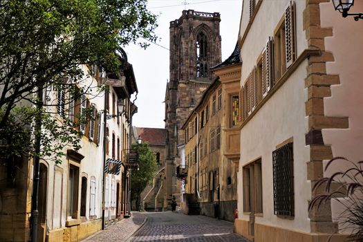 Beautiful street in the village of Rouffach, France with cobblestone street, residential houses and the Assumption Church