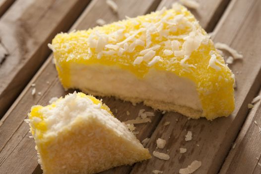 Lemon flavored lamington on sponge cake cut open to show the cake inside with coconut crumbs on a wooden table