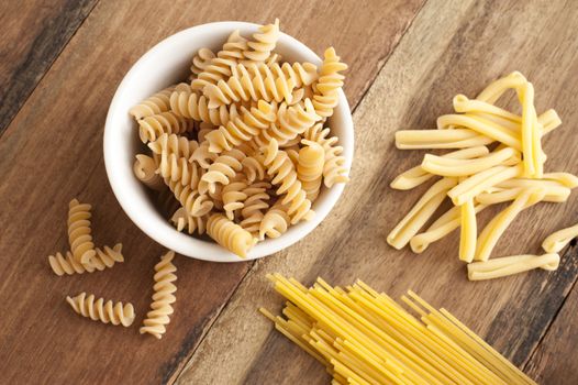 Assortment of dried Italian pasta on wood with spiral fusilli in a bowl and spaghetti viewed from above