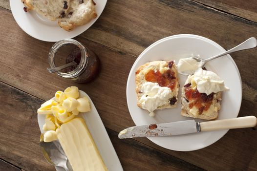 Buttered fruity rock cakes with jam and whipped cream served on a plate with a knife in an overhead view