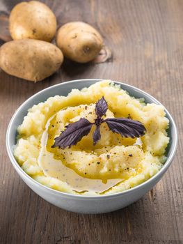 Mashed potatoes with fresh red basil in blue bowl on wooden background. Copy space.